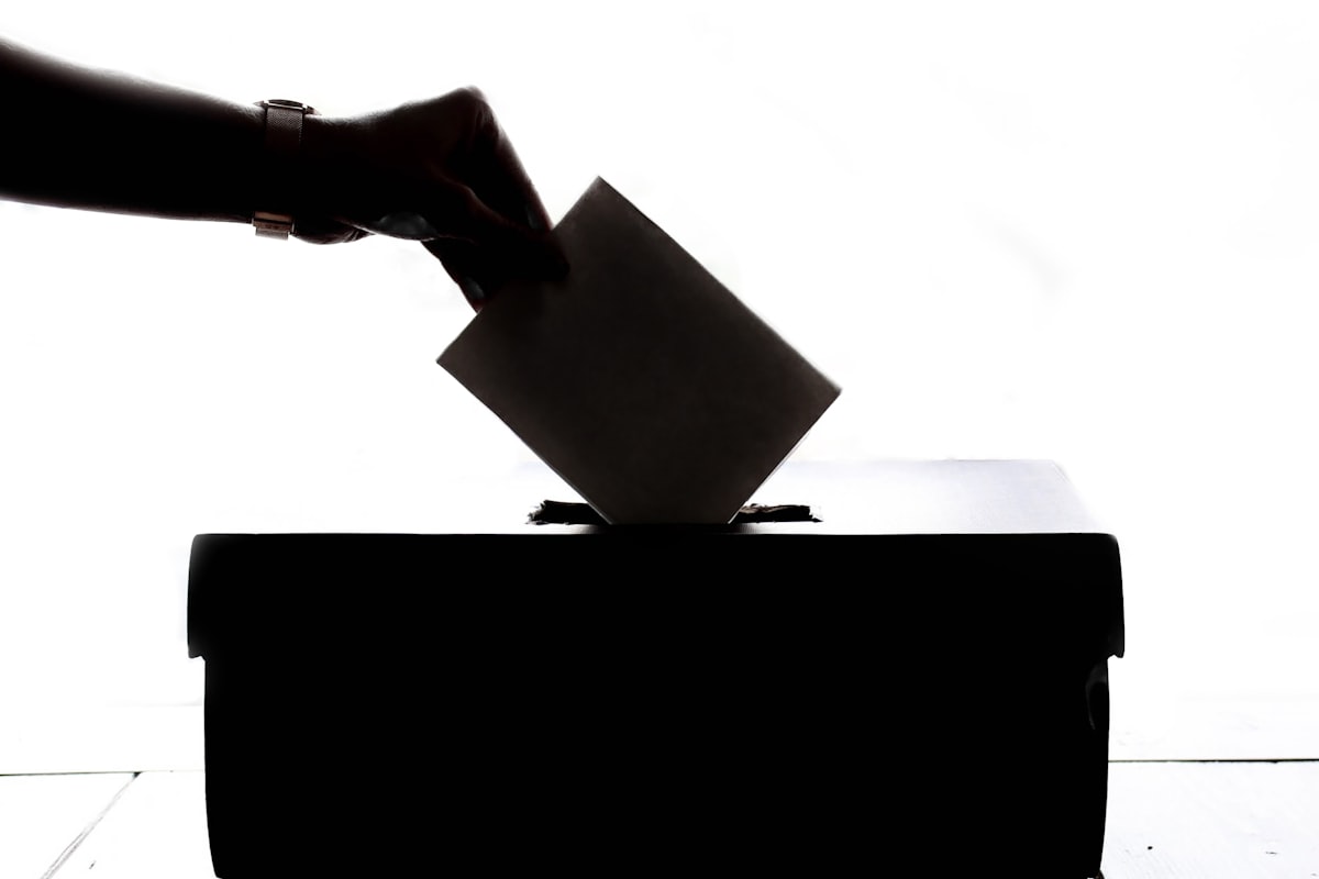 A hand placing a ballot into a ballot box, in silhouette